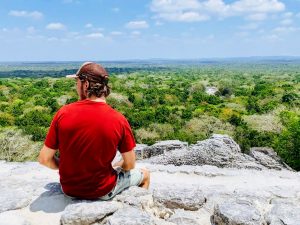 Damien à Calakmul assis sur un rocher avec la jungle et des ruines Mayas en arrière plan